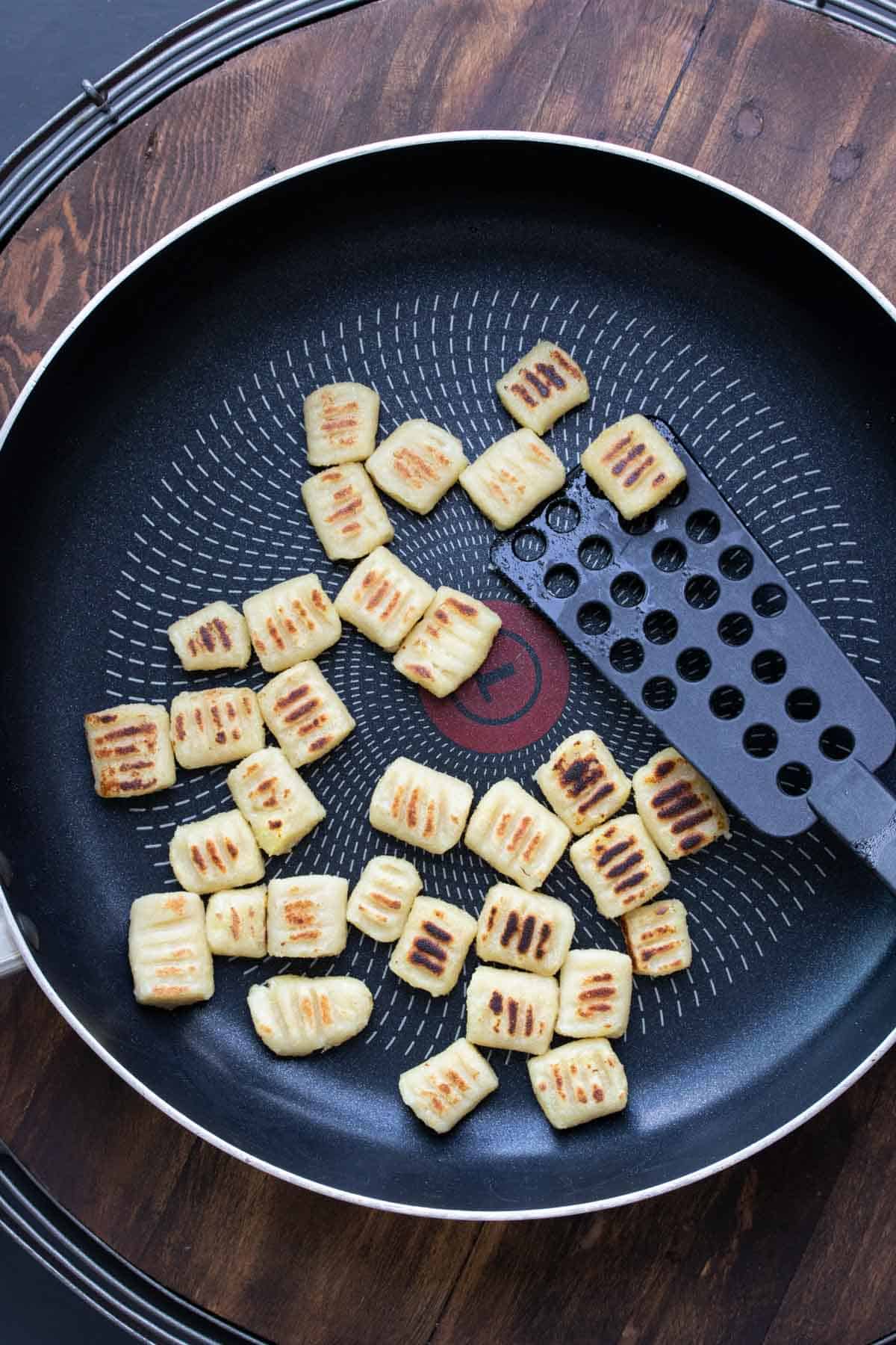 Gnocchi being sautéed to crispy in a pan.