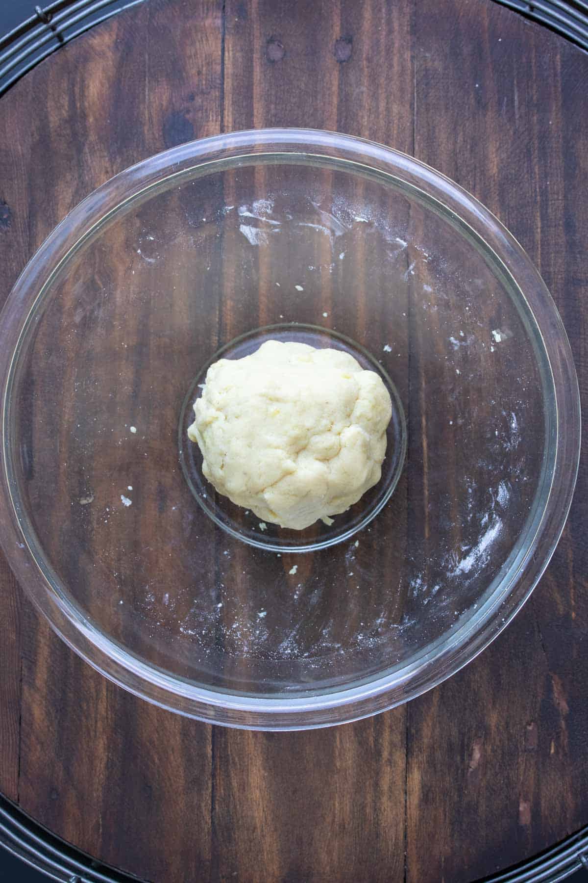 Glass bowl on a wooden surface with a ball of dough inside.