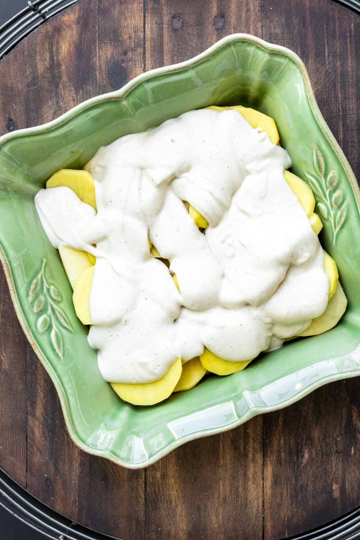 Green baking dish with sliced potatoes covered in creamy drizzle.