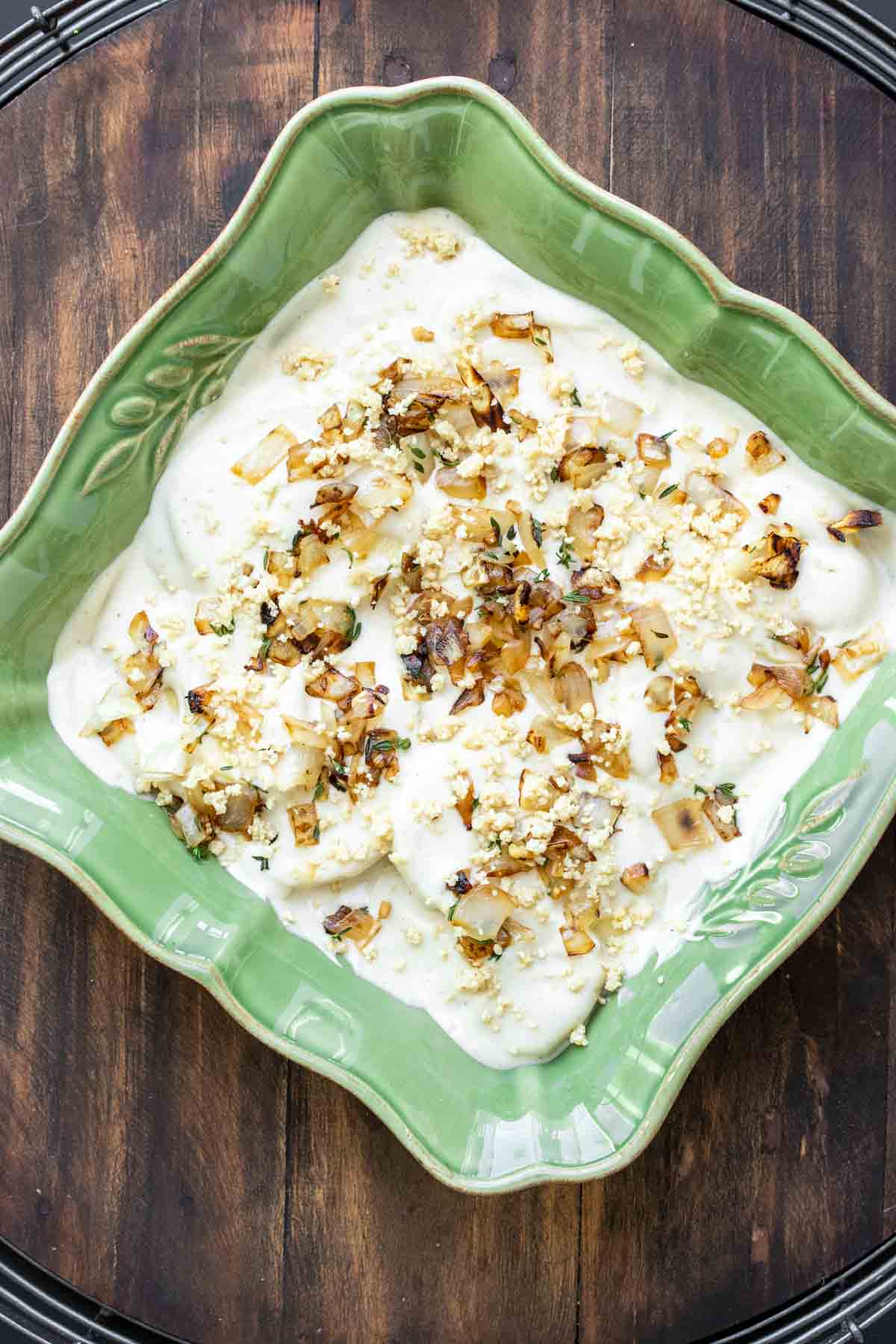 Green baking dish with creamy sauce topped with sautéed onions.
