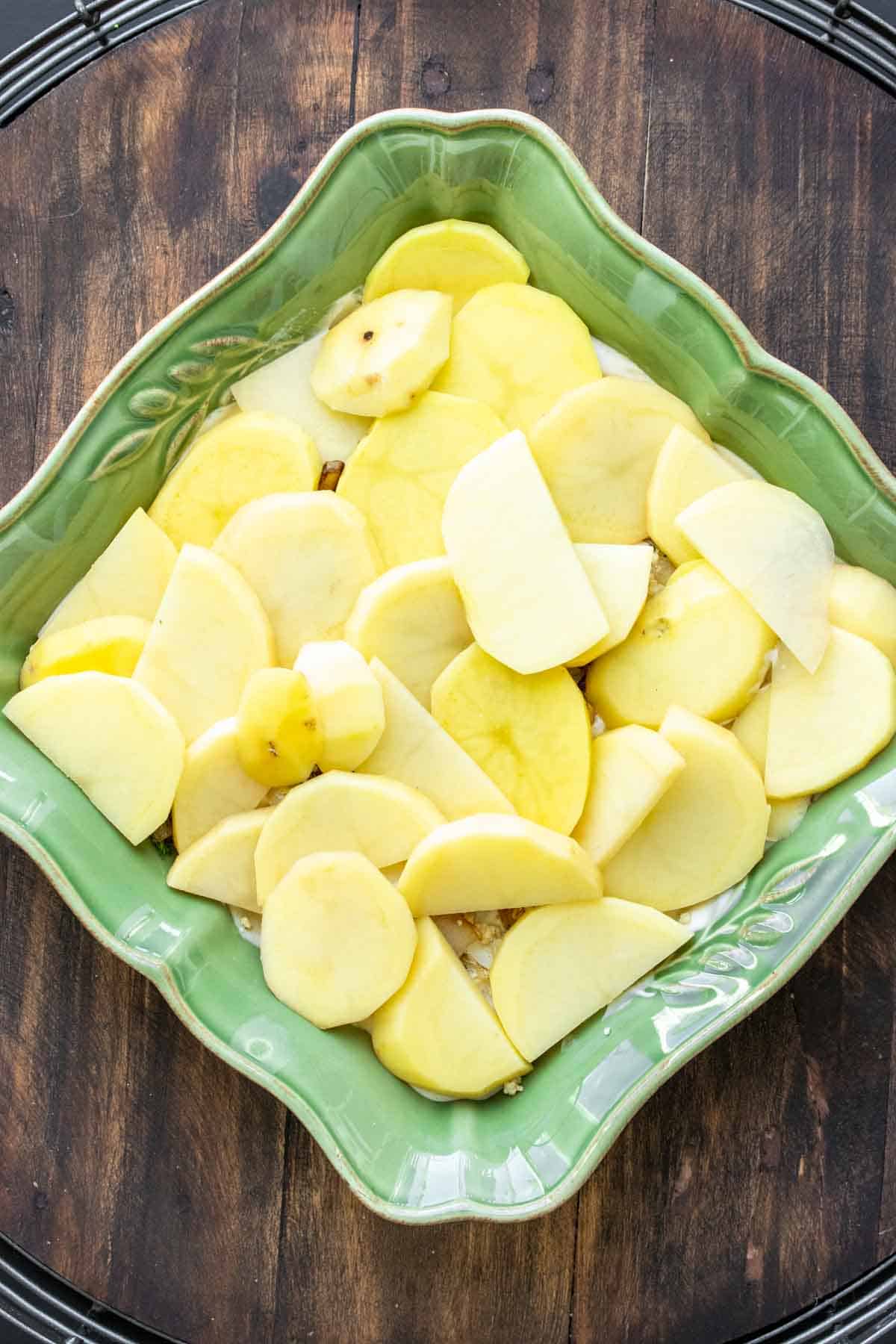 Green baking dish with slices of potatoes in it.