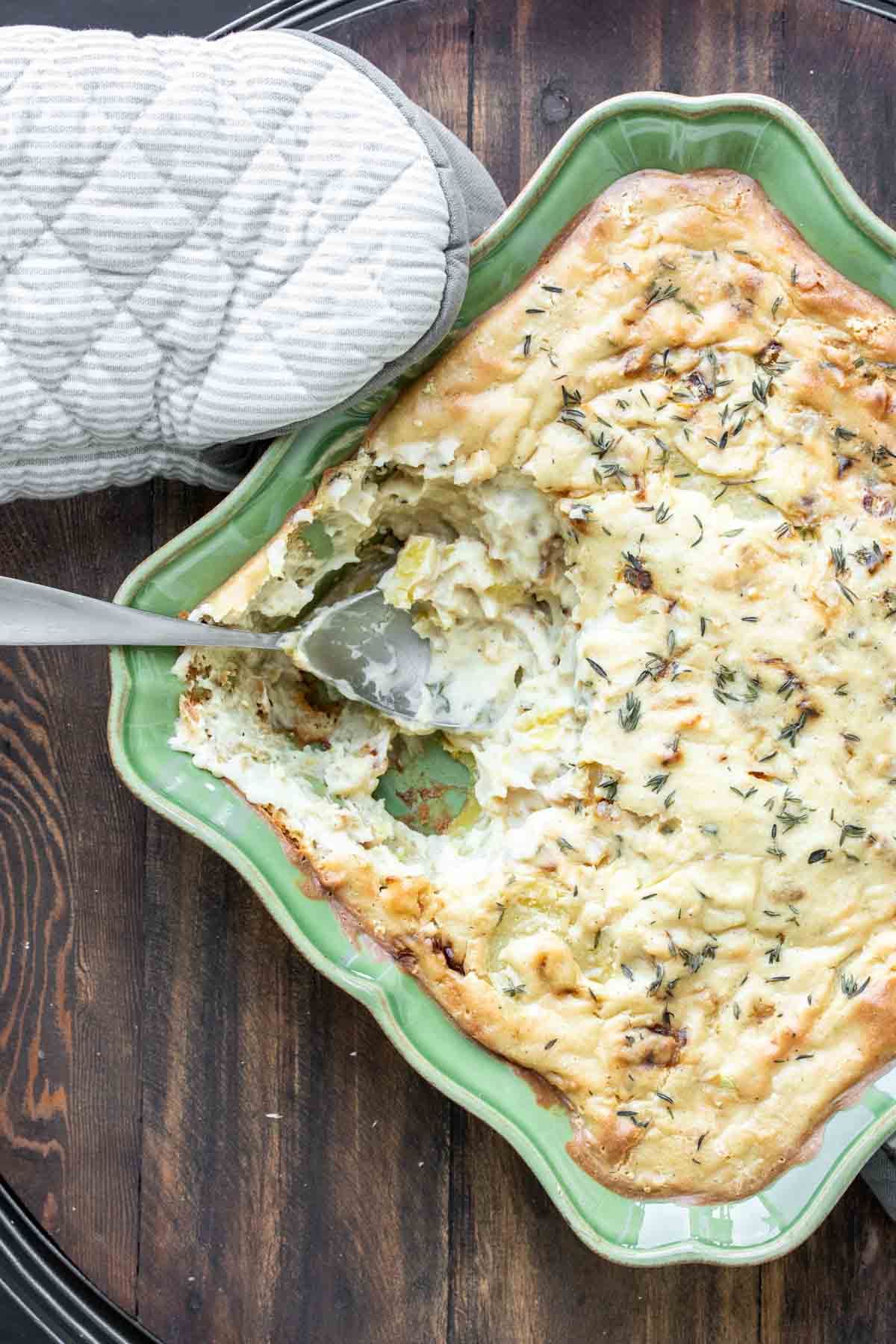 Spoon getting a scoop of scalloped potatoes from a green baking dish.