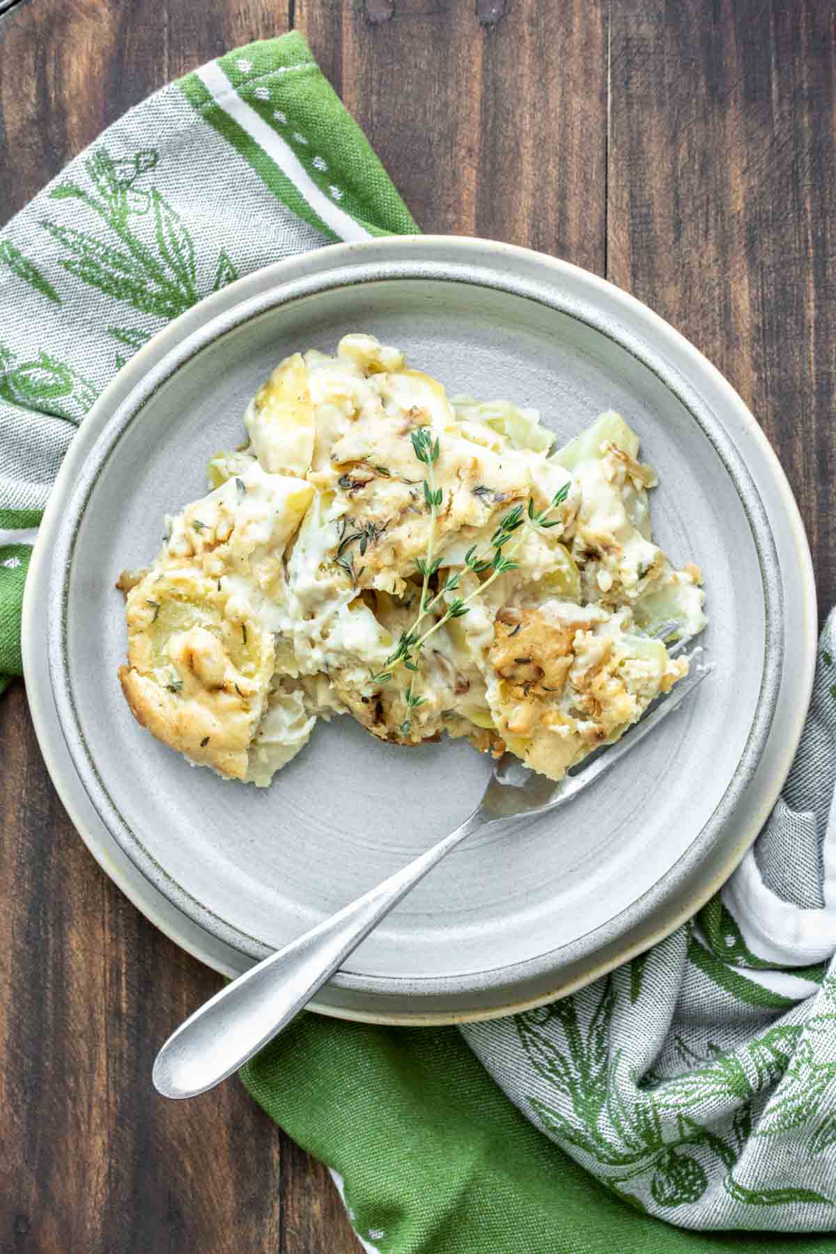 Grey plate with scalloped potatoes on it and a sprig of thyme