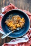 A photo of a serving of sweet potato casserole with pecan topping on a blue plate sitting on a blue striped towel.