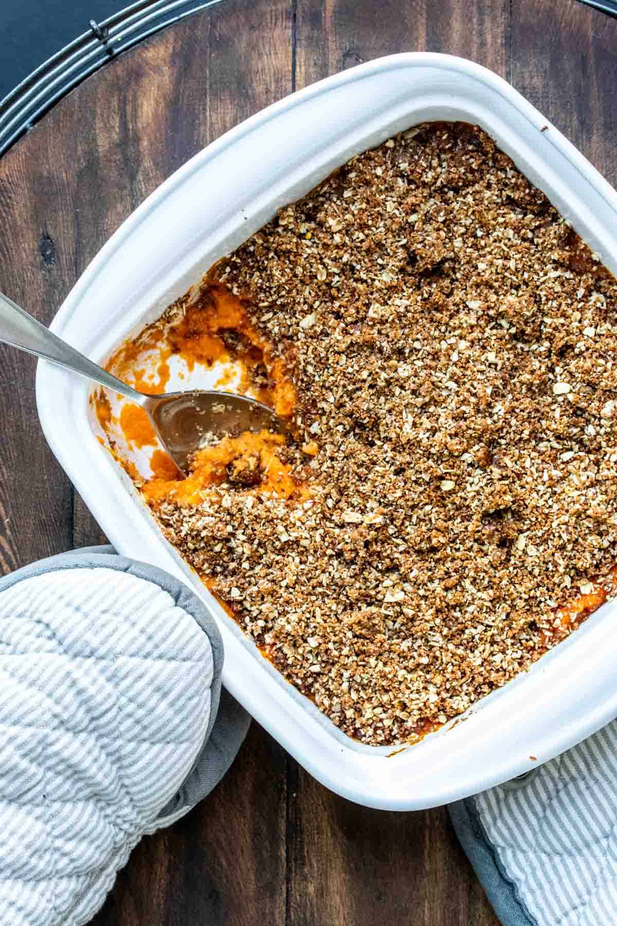 Spoon serving a baked sweet potato casserole in a white dish.