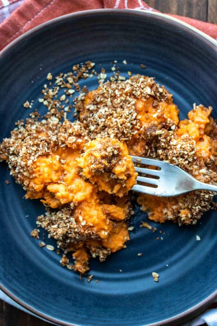 Fork getting a bite of sweet potato casserole from a blue plate.