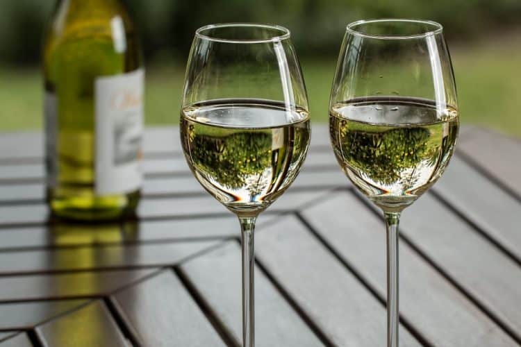 Two wine glasses on a table with white wine in them