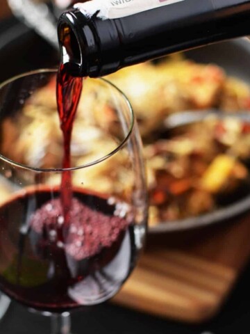 A wine glass with red wine being poured inside