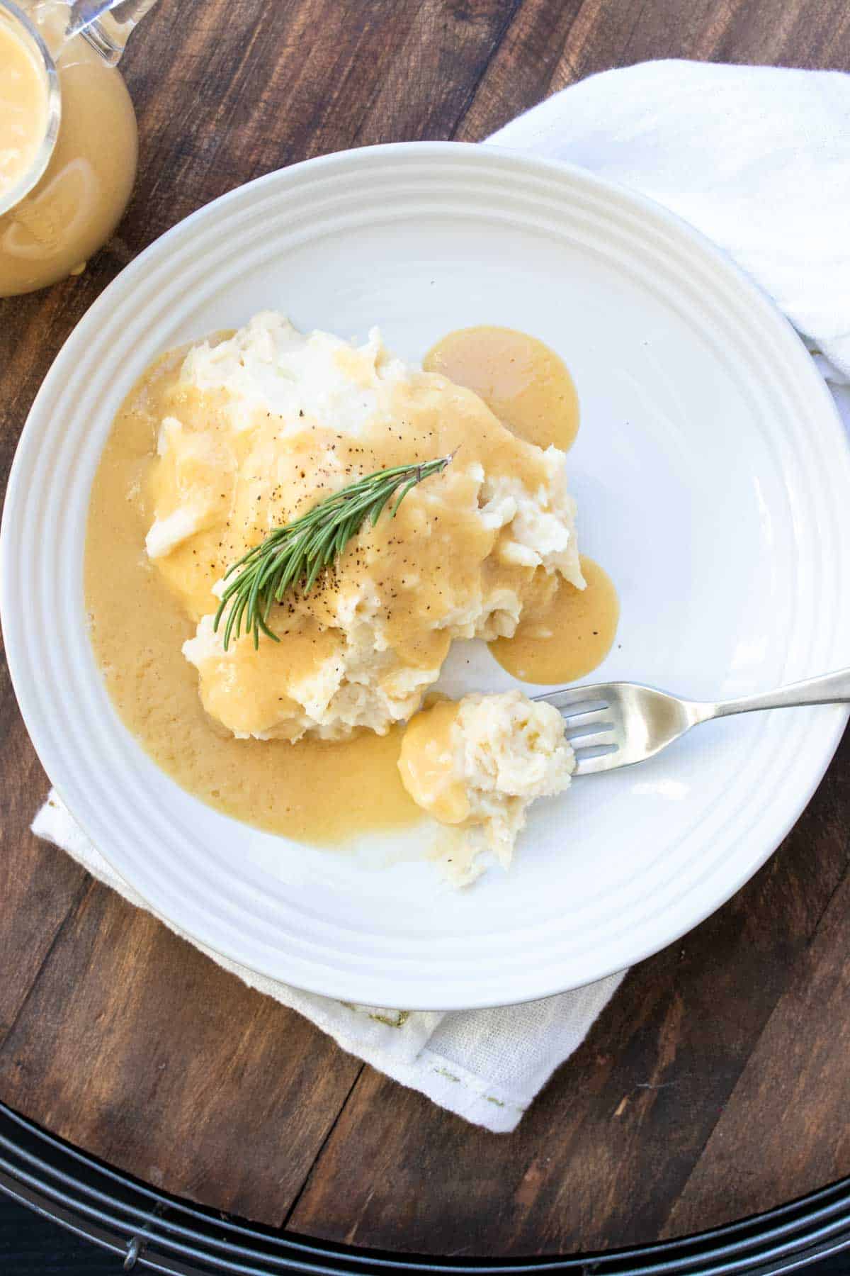Fork getting a bite from a white plate of mashed potatoes and gravy