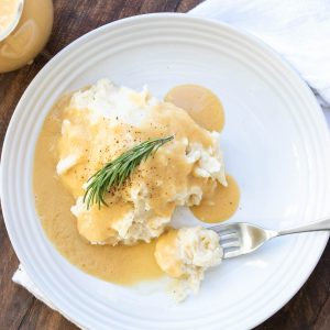 Gravy over a pile of mashed potatoes on a white plate.