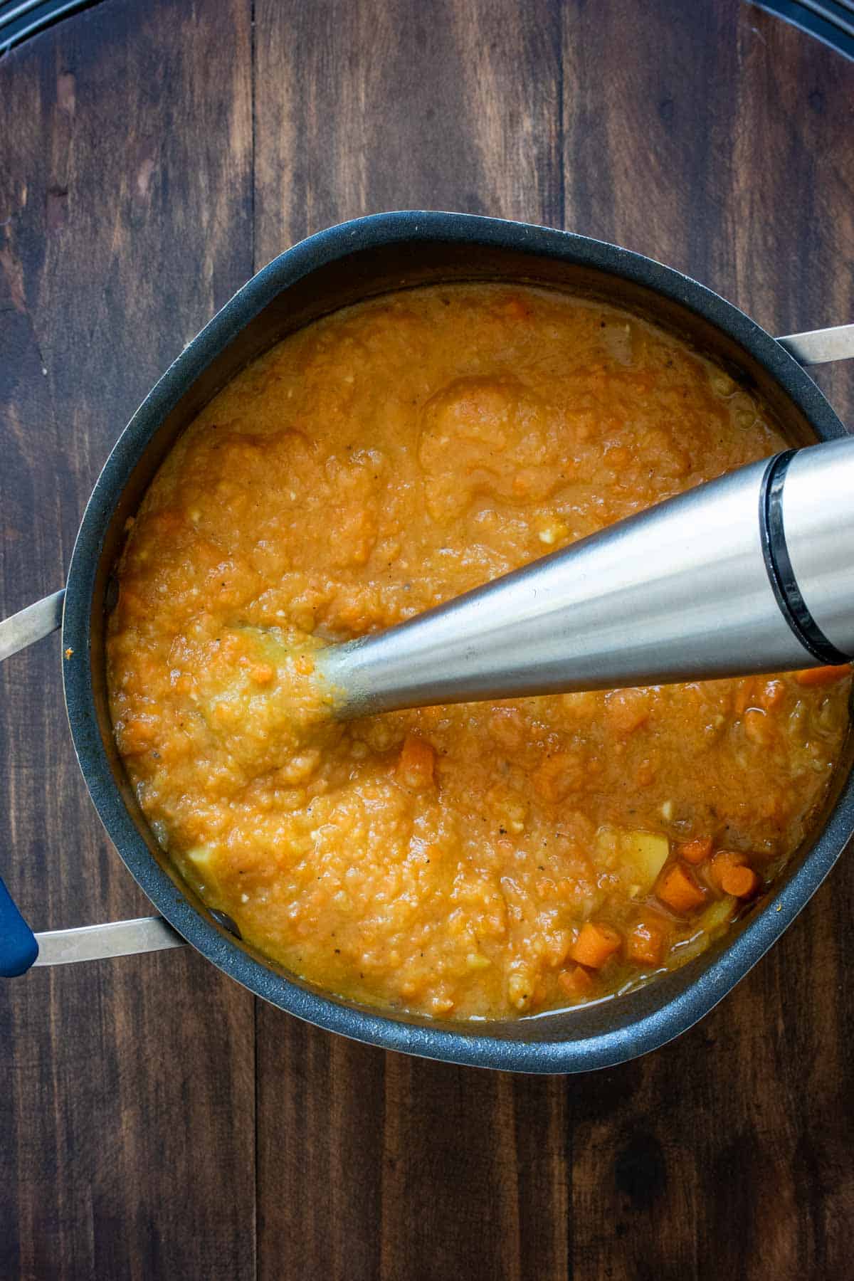 An immersion blender blending orange colored soup in a pot