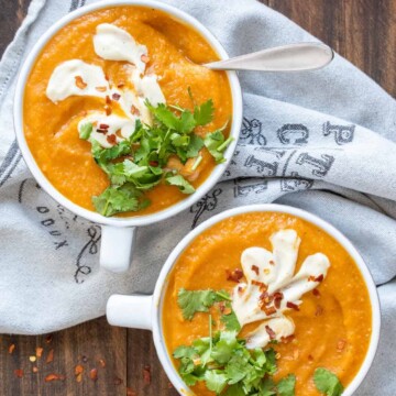 Two white bowls filled with carrot soup and topped with cilantro and cream