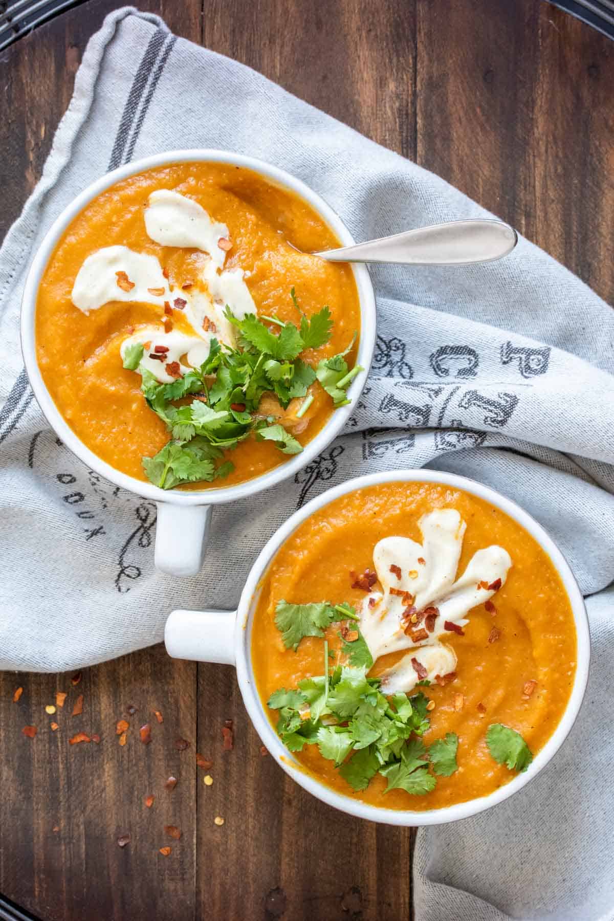 Two white bowls filled with carrot soup and topped with cilantro and cream