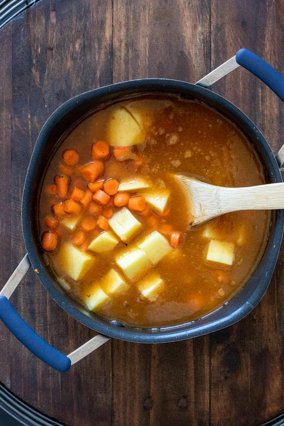 Wooden spoon mixing soup with carrots and potatoes