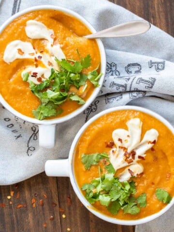 Two white soup bowls filled with carrot soup