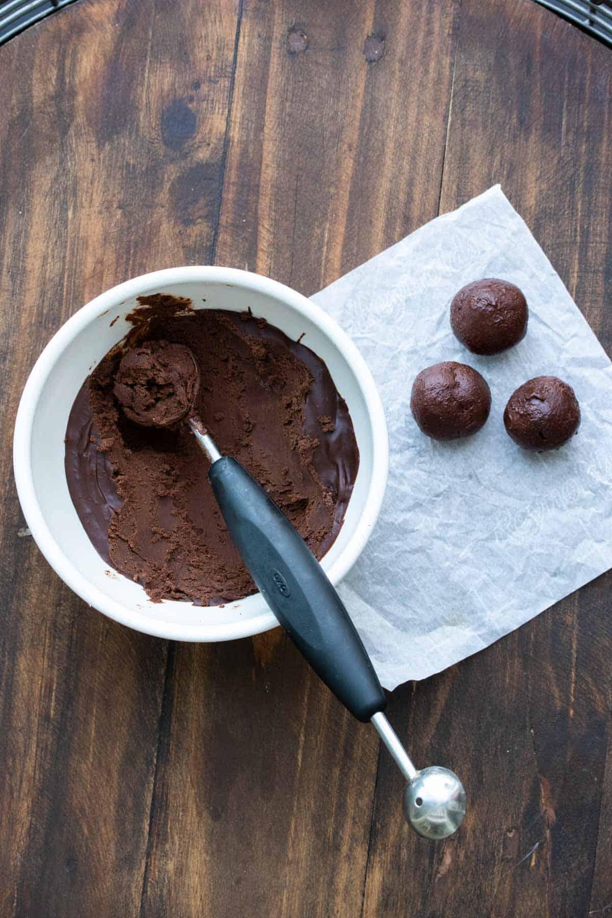 Bowl of truffle mixture and balls of it on a piece of parchment