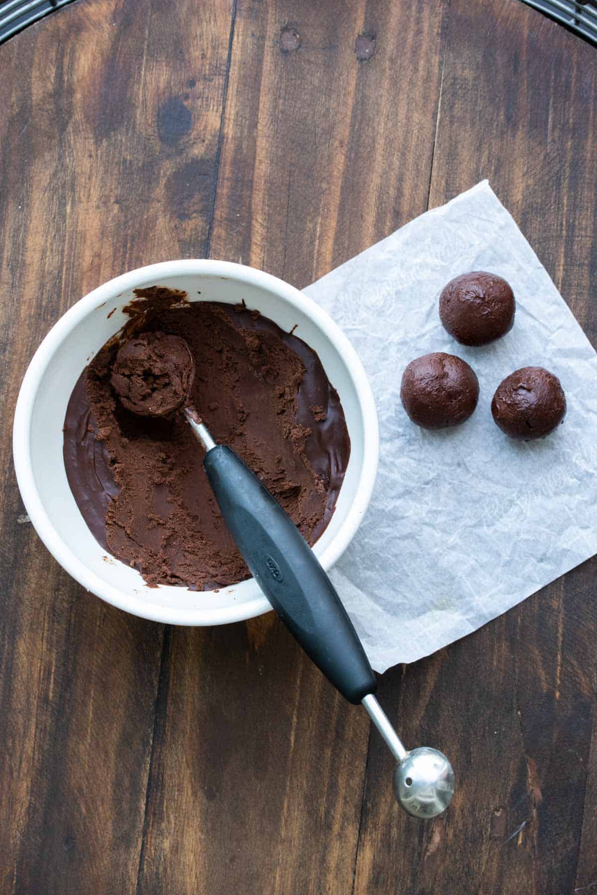 Bowl of truffle mixture and balls of it on a piece of parchment.