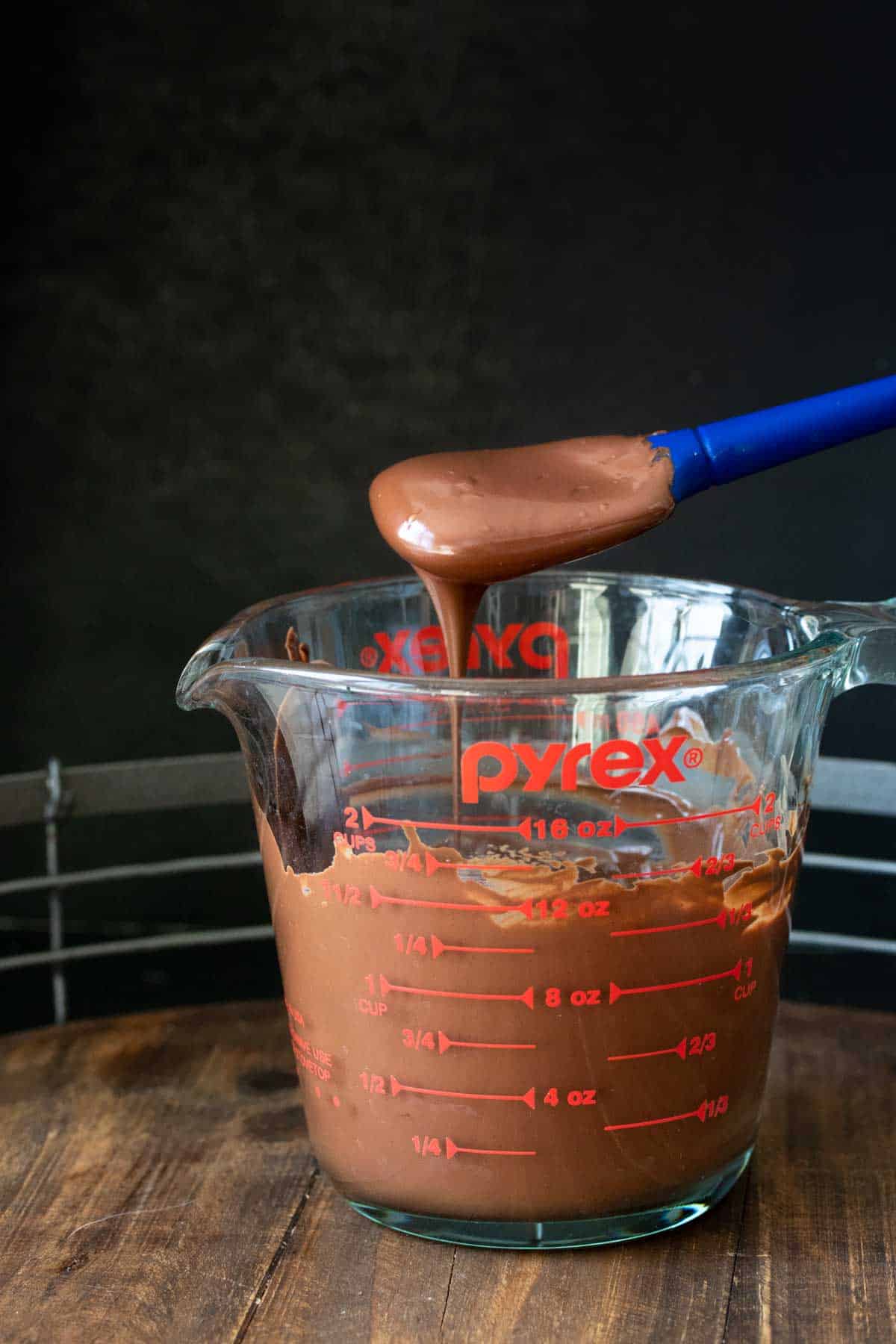 Spatula dripping with melted chocolate on top of a glass pyrex