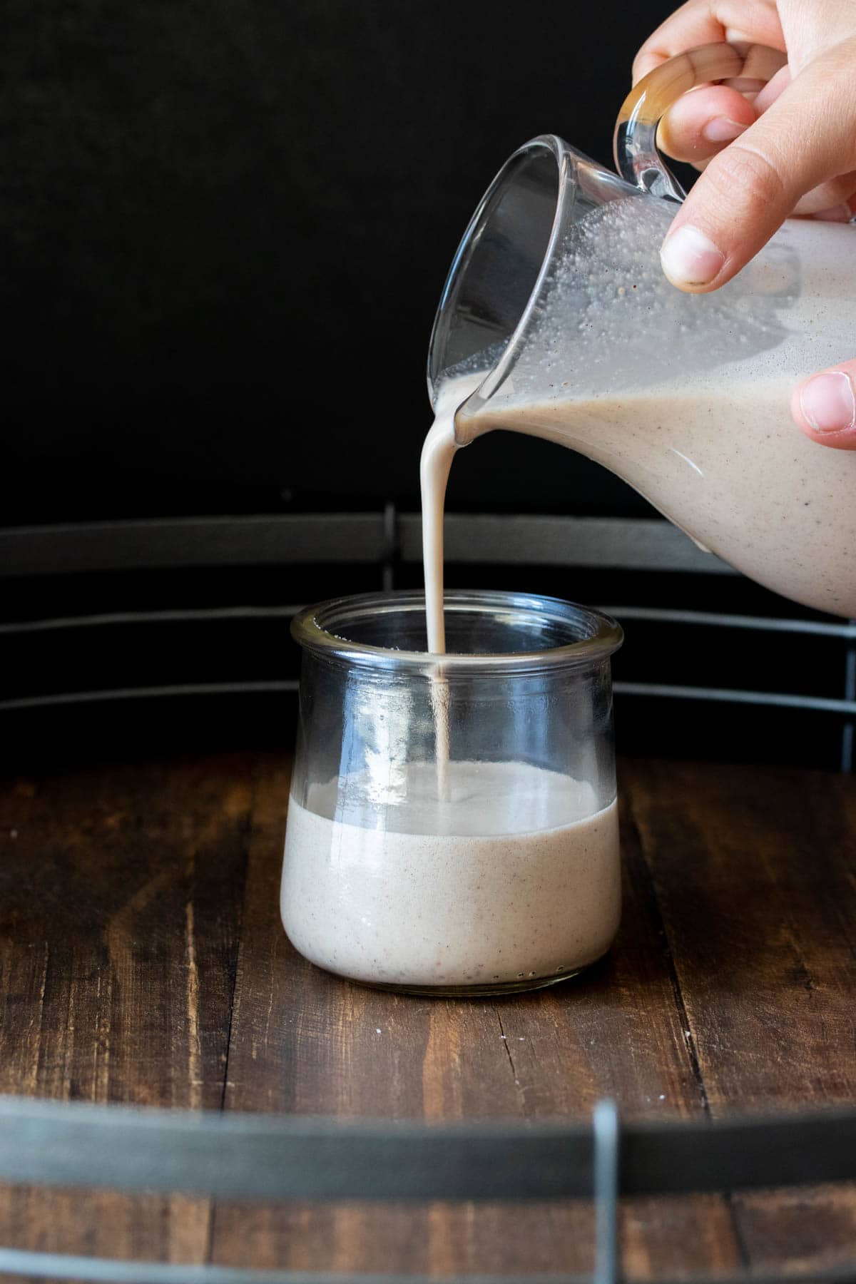 Someone pouring eggnog into a glass jar.