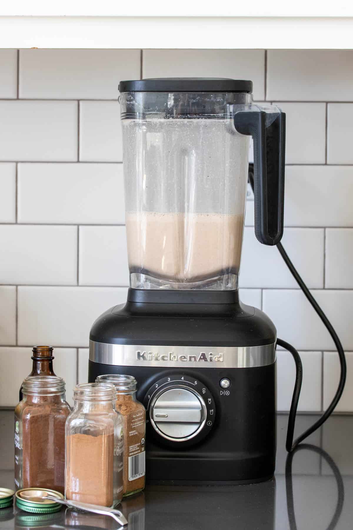 Blender filled with eggnog and with spices in front of it.