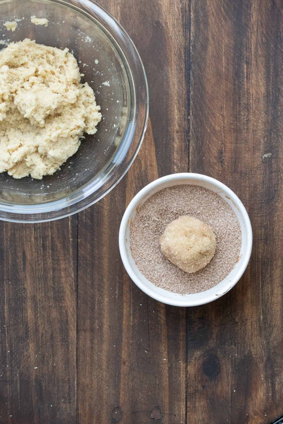 Ball of raw snickerdoodle dough in a bowl of cinnamon sugar coating