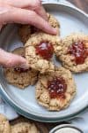 Hand taking a thumbprint cookie with a bite out of it from a pile