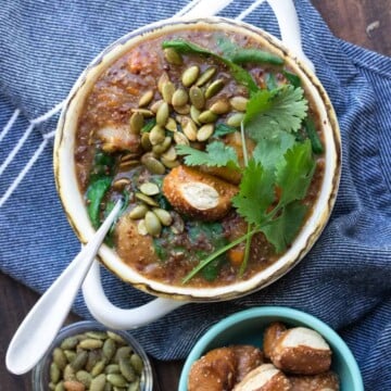 White soup bowl with sweet potato soup and covered with cilantro, pretzels and pumpkin seeds