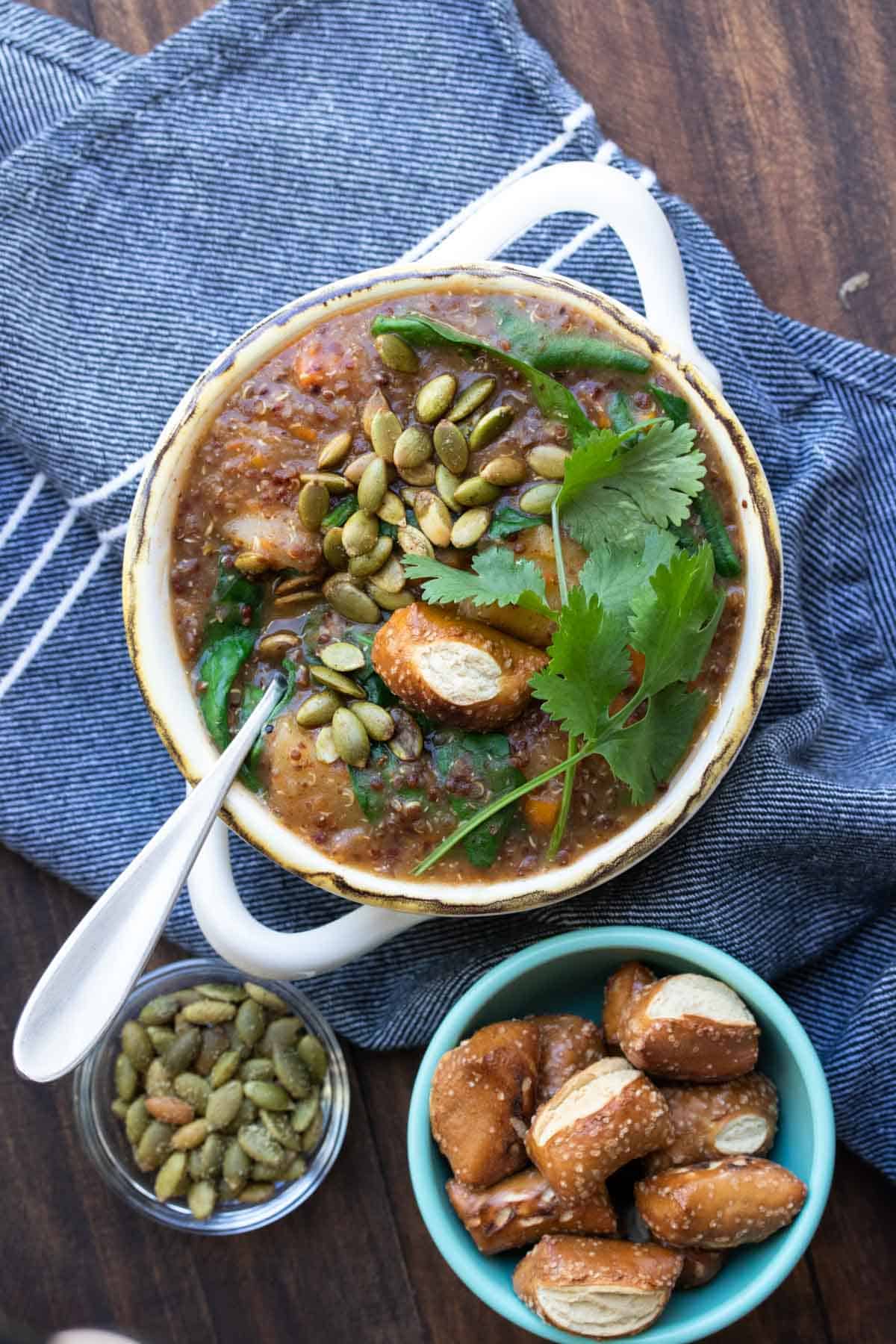 White soup bowl with sweet potato soup and covered with cilantro, pretzels and pumpkin seeds