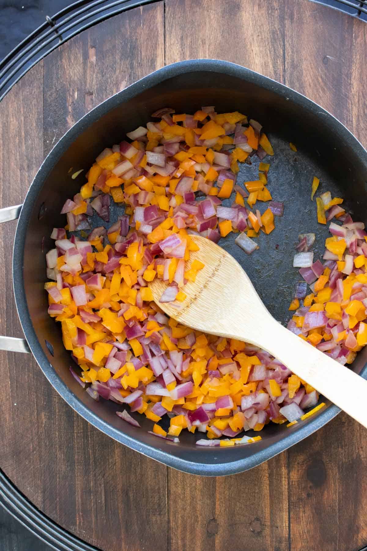 Carrots and onion being stirred in a pot by a wooden spoon