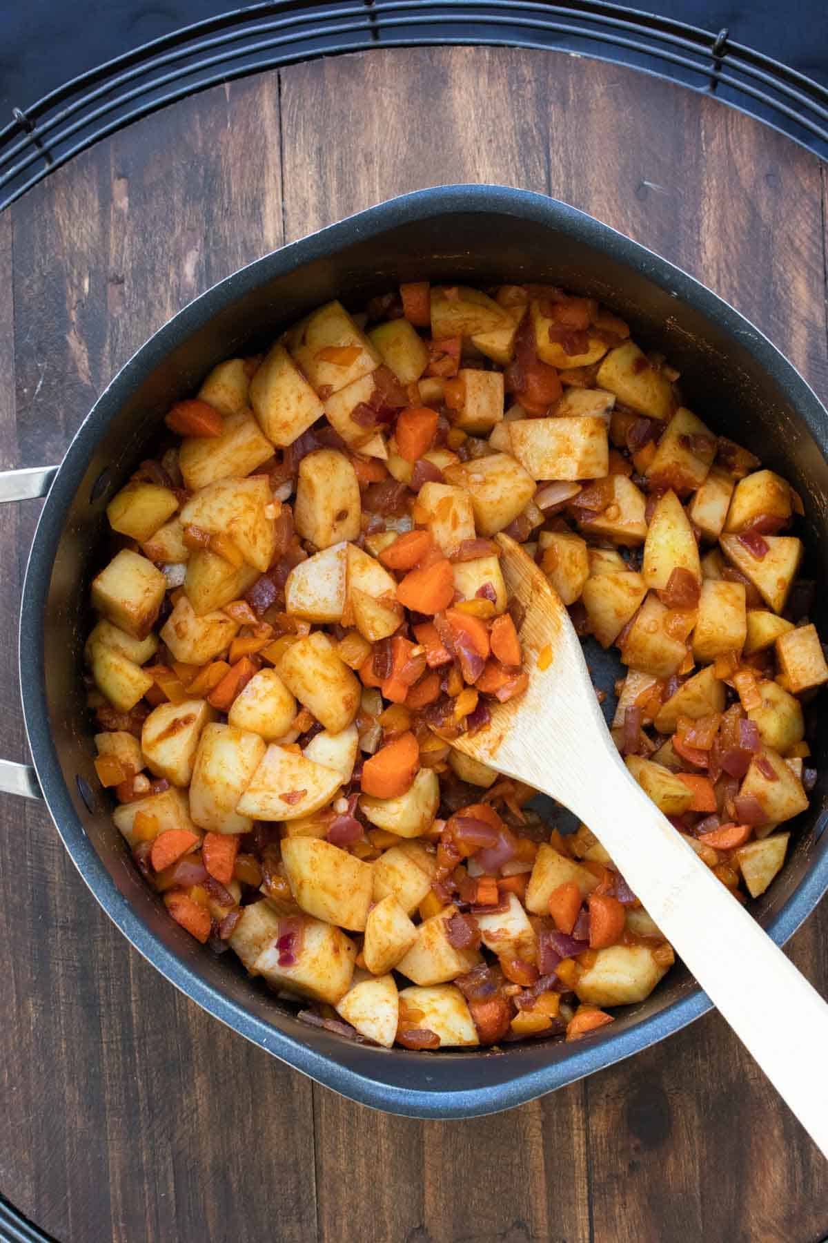 Wooden spoon stirring sweet potatoes, carrots and onion in a pot