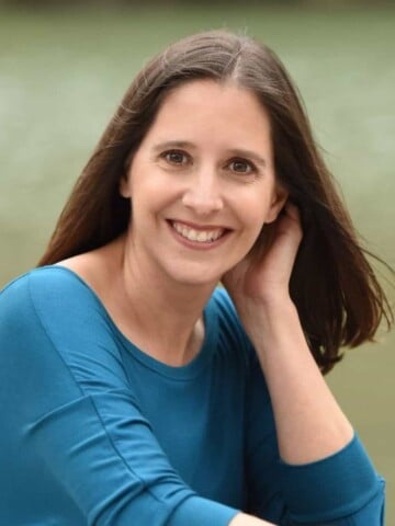 A woman in a blue long sleeve shirt with her hand behind her ear smiling