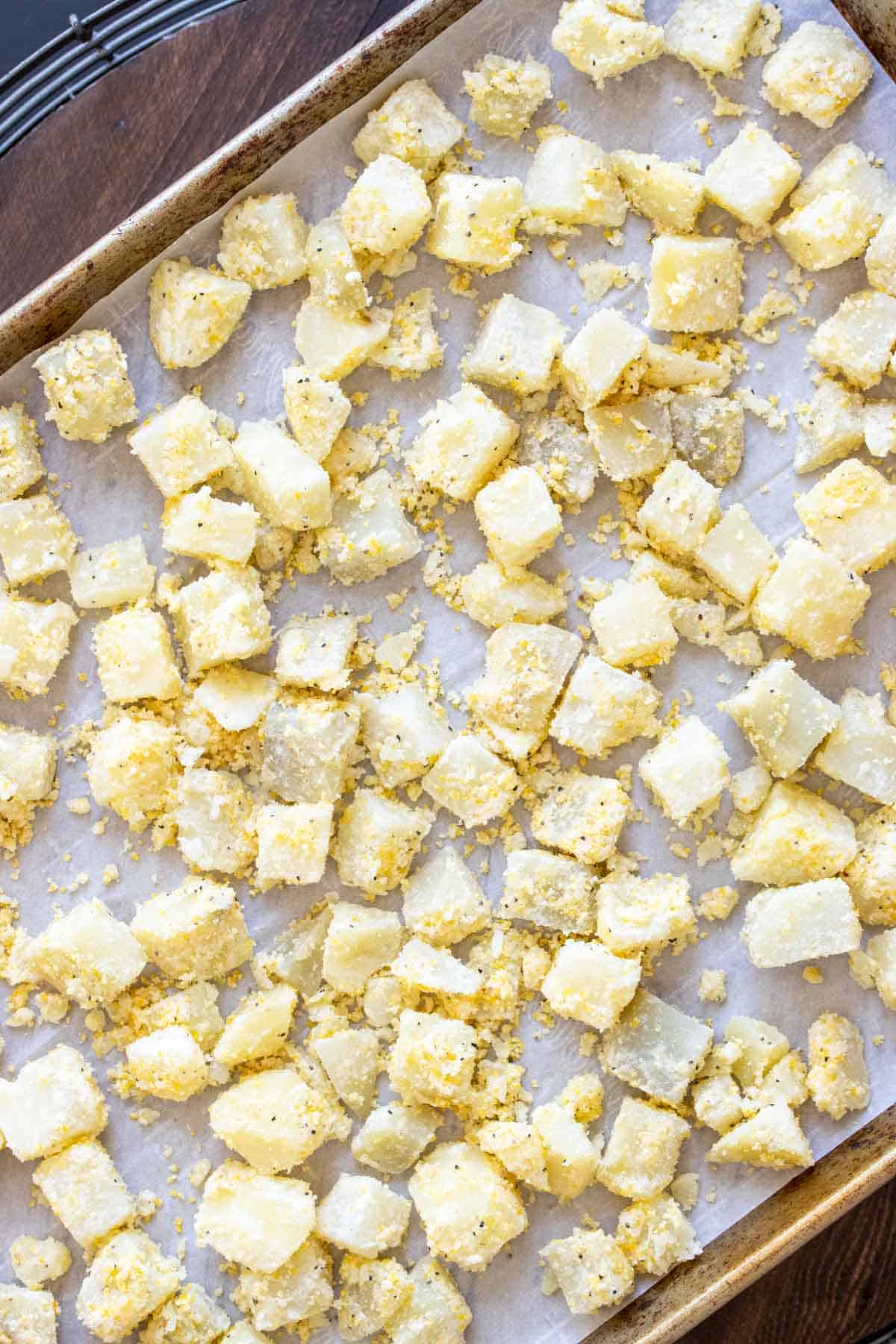 Coated potato cubes on a piece of parchment on a baking sheet