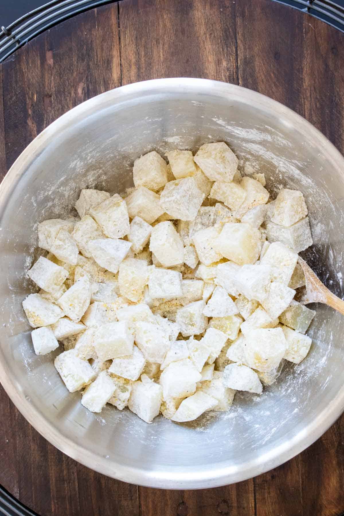 Metal bowl with cubed potatoes covered in crispy coating