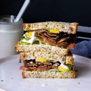 Two halves of a vegan BLT stacked on a plate