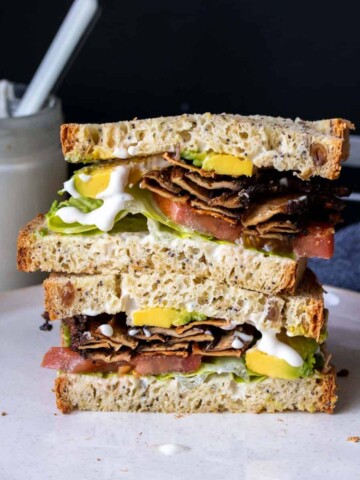 A vegan BLT sandwich cut in half and stacked on a plate