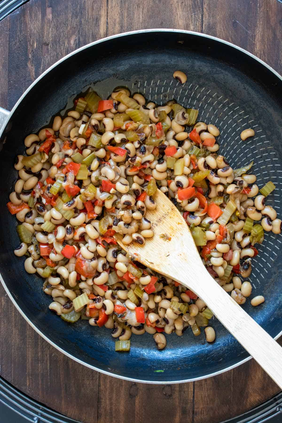 Sautéed veggies and black eyed peas being stirred by a wooden spoon