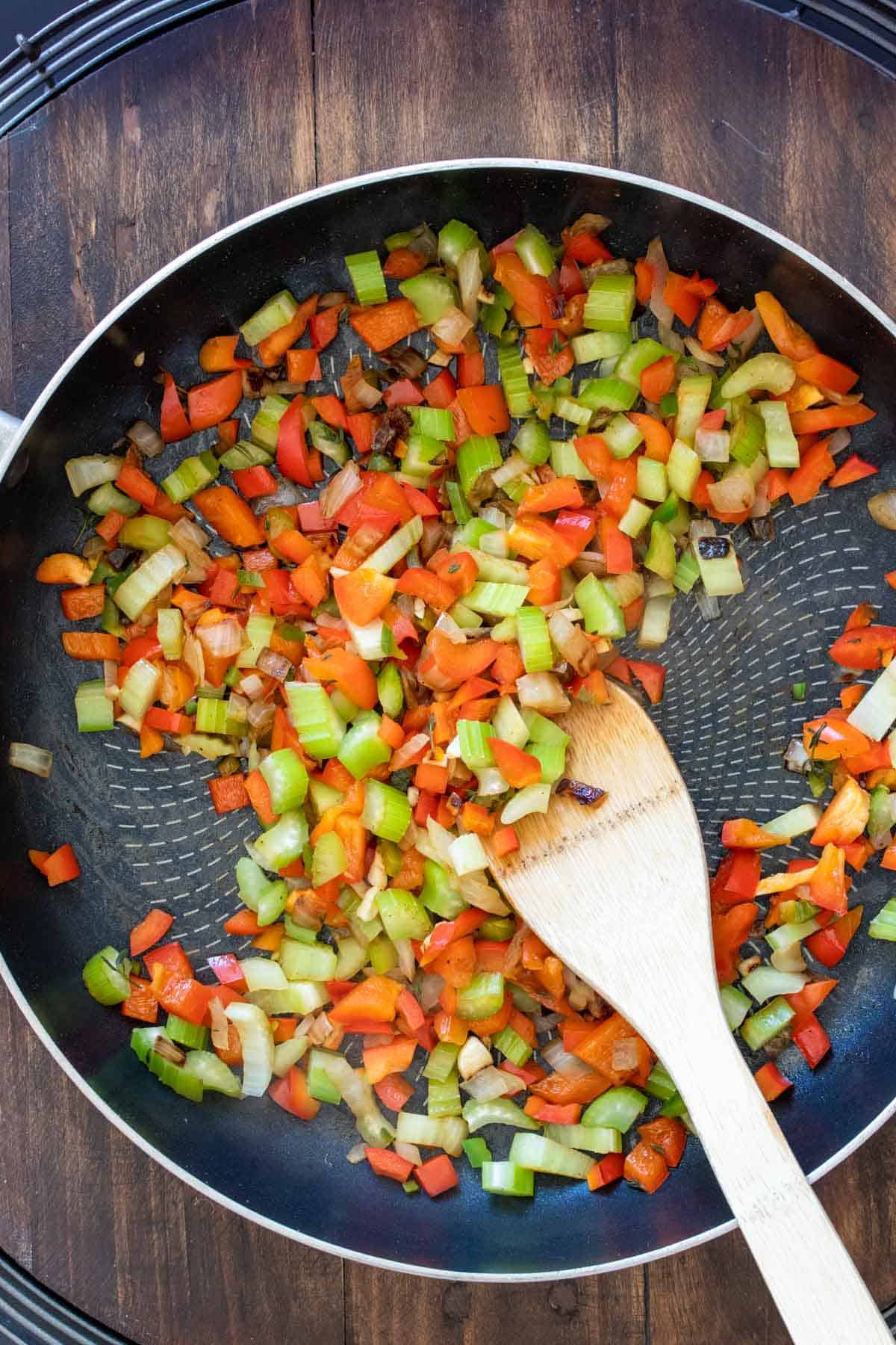 Wooden spoon stirring chopped veggies in a pan