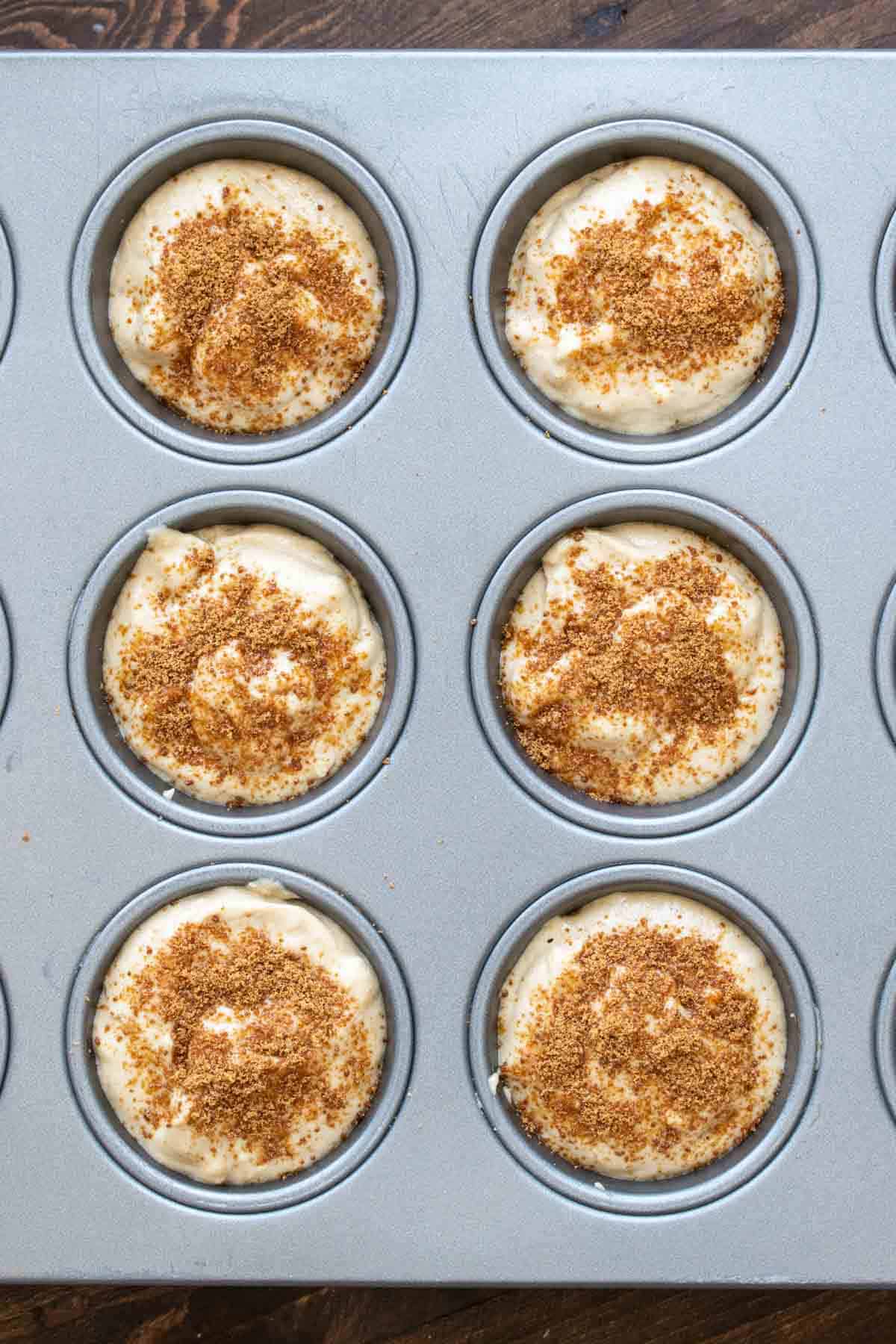 A muffin tin filled with muffin batter sprinkled with coconut sugar