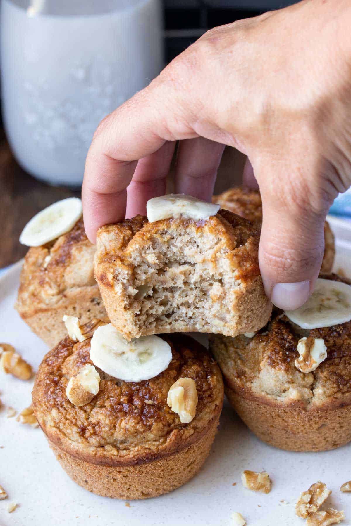 A hand holding a banana walnut muffin with a bite out of it