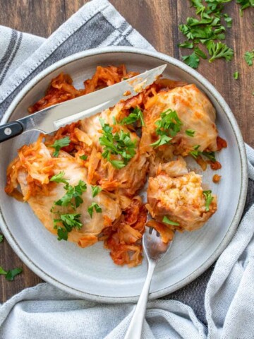 Cabbage rolls on a grey plate covered on tomato sauce and sprinkled with parsley.