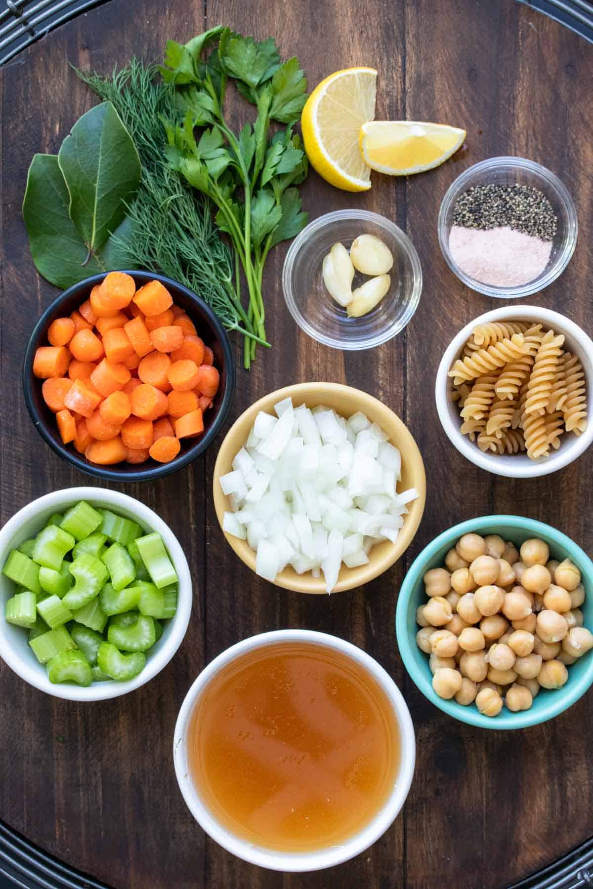 Different color and size bowls filled with all the ingredients for a chickpea veggie noodle soup