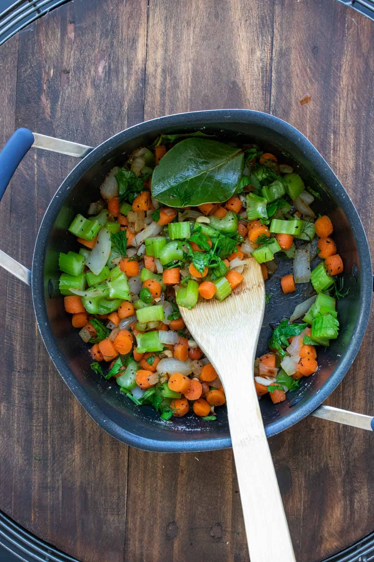 Wooden spoon sautéing veggies in a pot