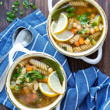 Two white soup bowls filled with chickpea veggie noodle soup