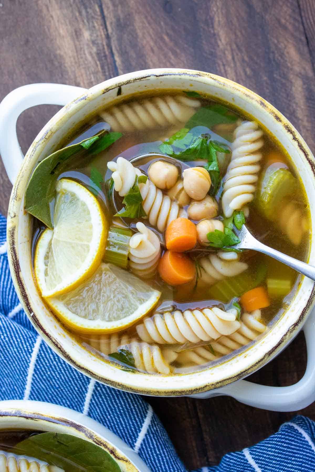 Spoon getting a bite of chickpea veggie noodle soup from a bowl