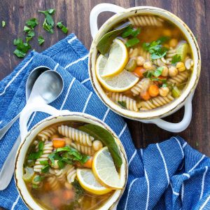 Veggie, chickpea and noodle soup in two soup bowls on a wooden surface.