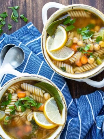 Veggie, chickpea and noodle soup in two soup bowls on a wooden surface.