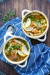Two white soup bowls filled with a veggie, chickpea and noodle soup on a blue towel
