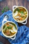 Two white soup bowls filled with a veggie, chickpea and noodle soup on a blue towel.