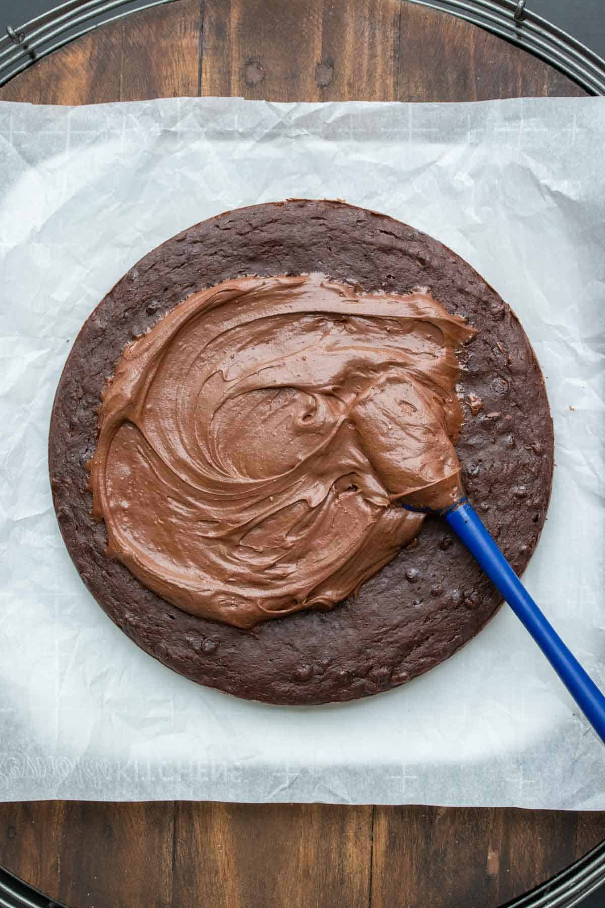 Top view of a spatula spreading frosting on a round chocolate cake