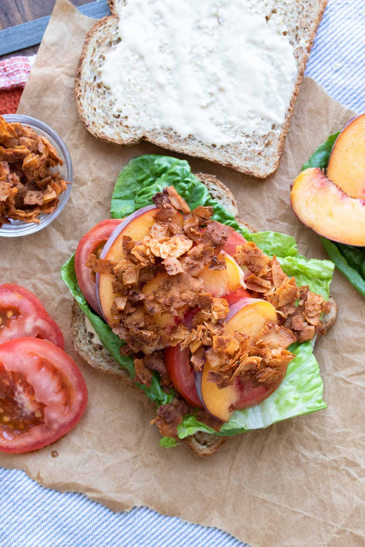 Top view of an open faced sandwich with lettuce, tomatoes, peaches and coconut bacon